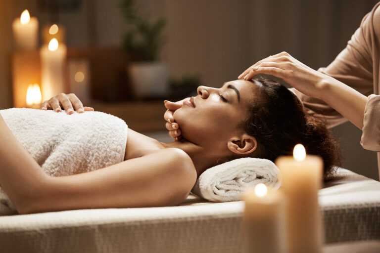 Attractive african girl enjoying face massage in spa salon